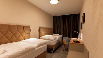 A hotel room with two beds, a desk with a chair, a lamp, and a small table with fruits.