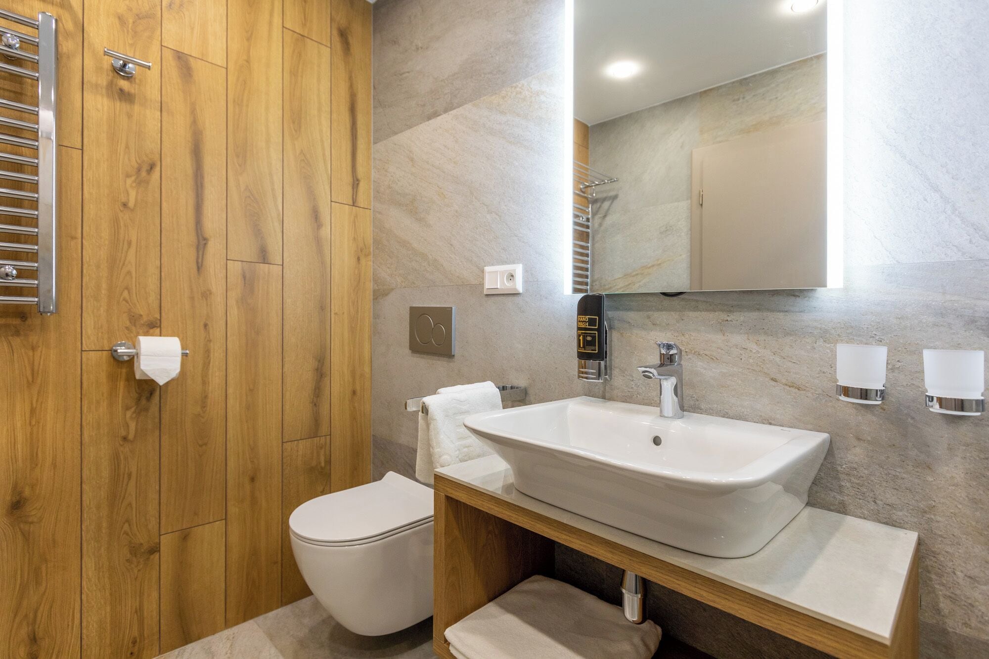A modern bathroom with a wooden vanity, a white sink, and a toilet.
