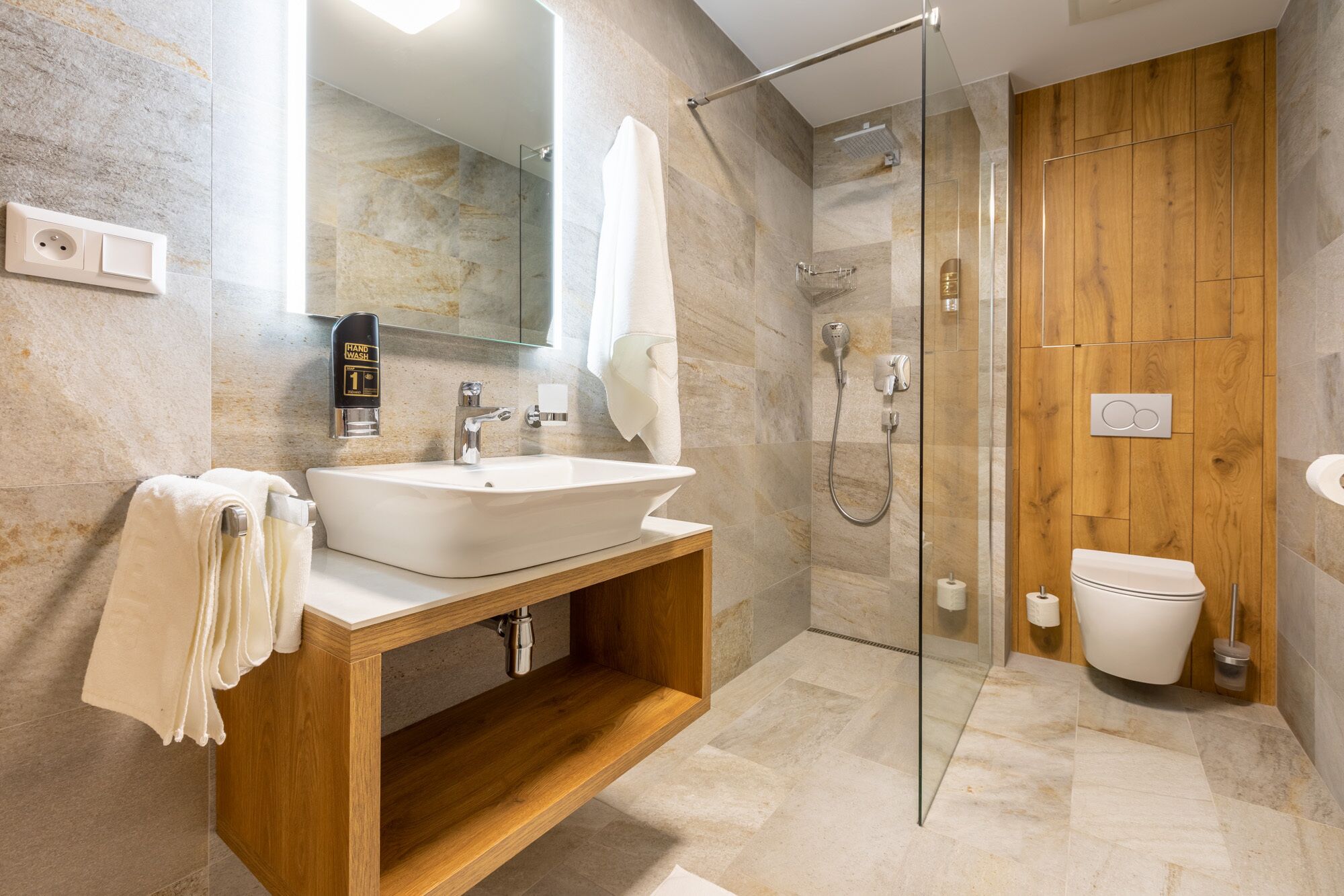 Un baño moderno con ducha de vidrio, tocador de madera y un espejo grande.