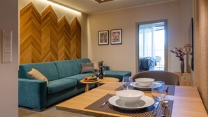 A modern living room with a teal sofa, wooden herringbone wall, and a dining area with a wooden table set for a meal. - APLEND Lake Resort  (Štrba)