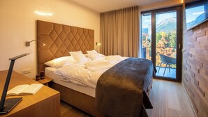 A modern hotel room with a large bed, a desk with a laptop, a chair, and a view of a mountainous landscape through the window. - APLEND Lake Resort  (Štrba)
