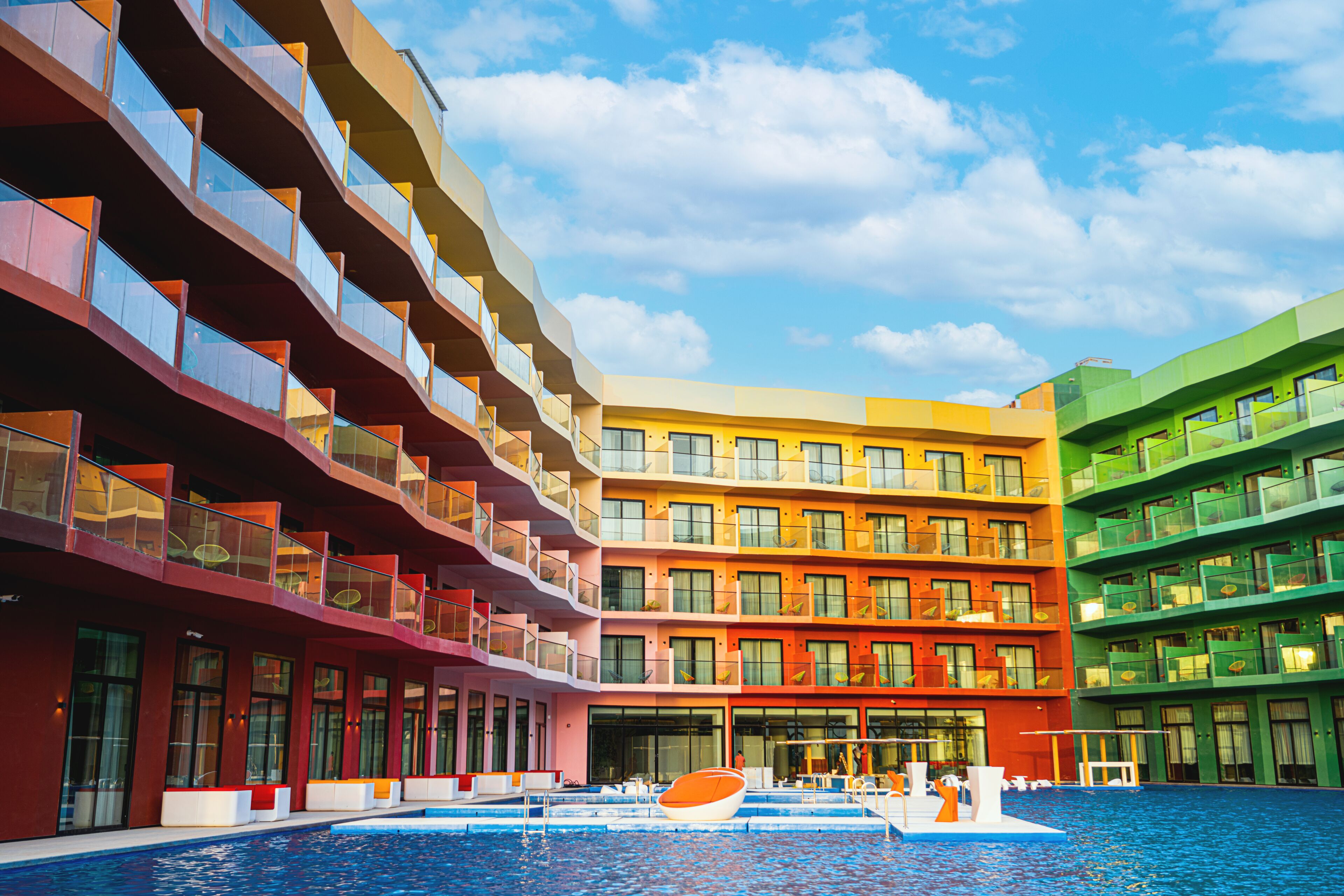 Un hôtel à plusieurs étages, doté de balcons, d’une piscine et offrant une vue sur un ciel dégagé.
