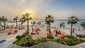 Un complejo turístico frente a la playa con tumbonas, palmeras y vistas al mar.