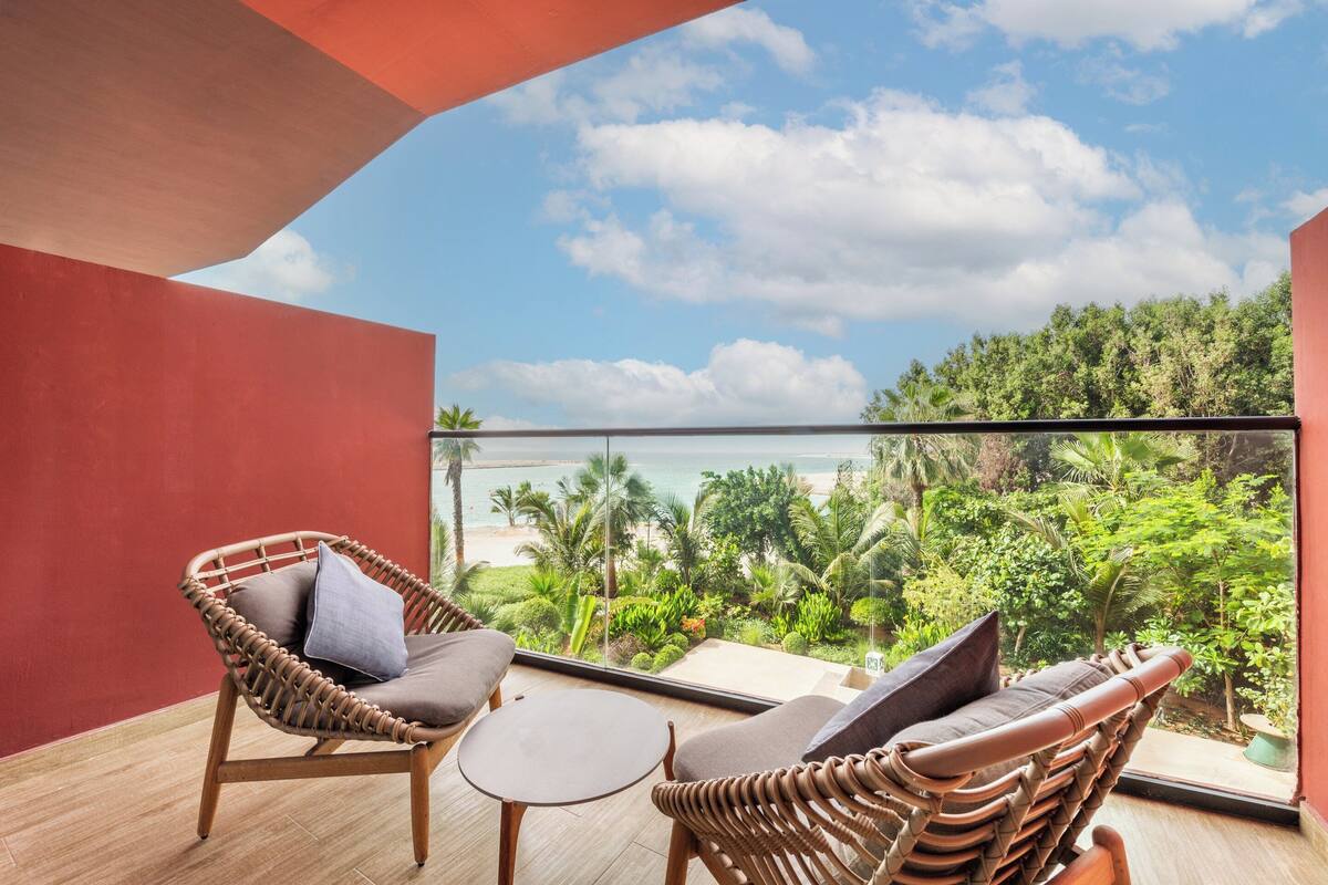 A balcony with wicker furniture and a view of the beach and greenery.
