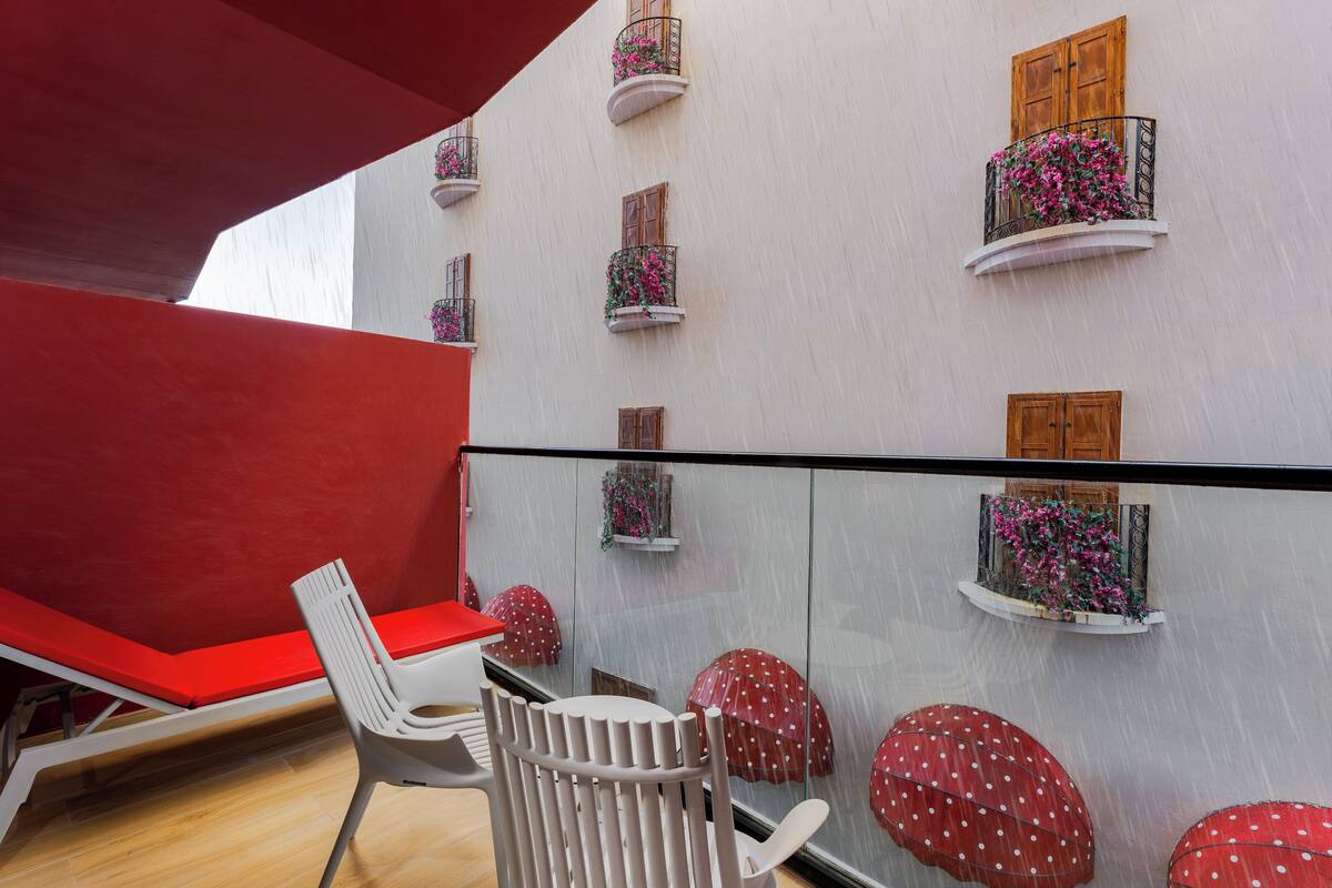 A modern interior with a red bench, white chairs, and a glass partition with red umbrellas.