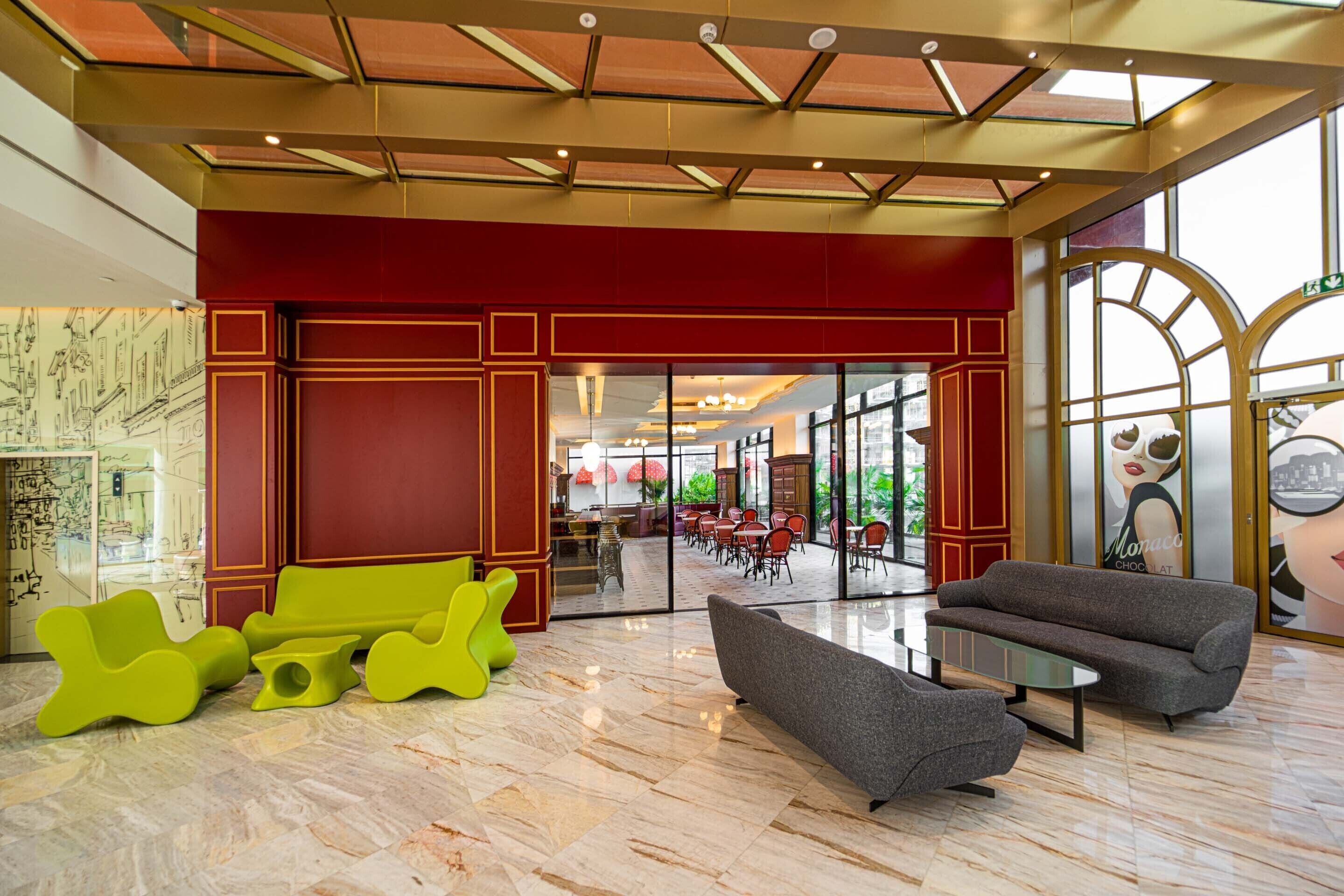 A lobby with a red wall, a glass door leading to a dining area, and modern seating.