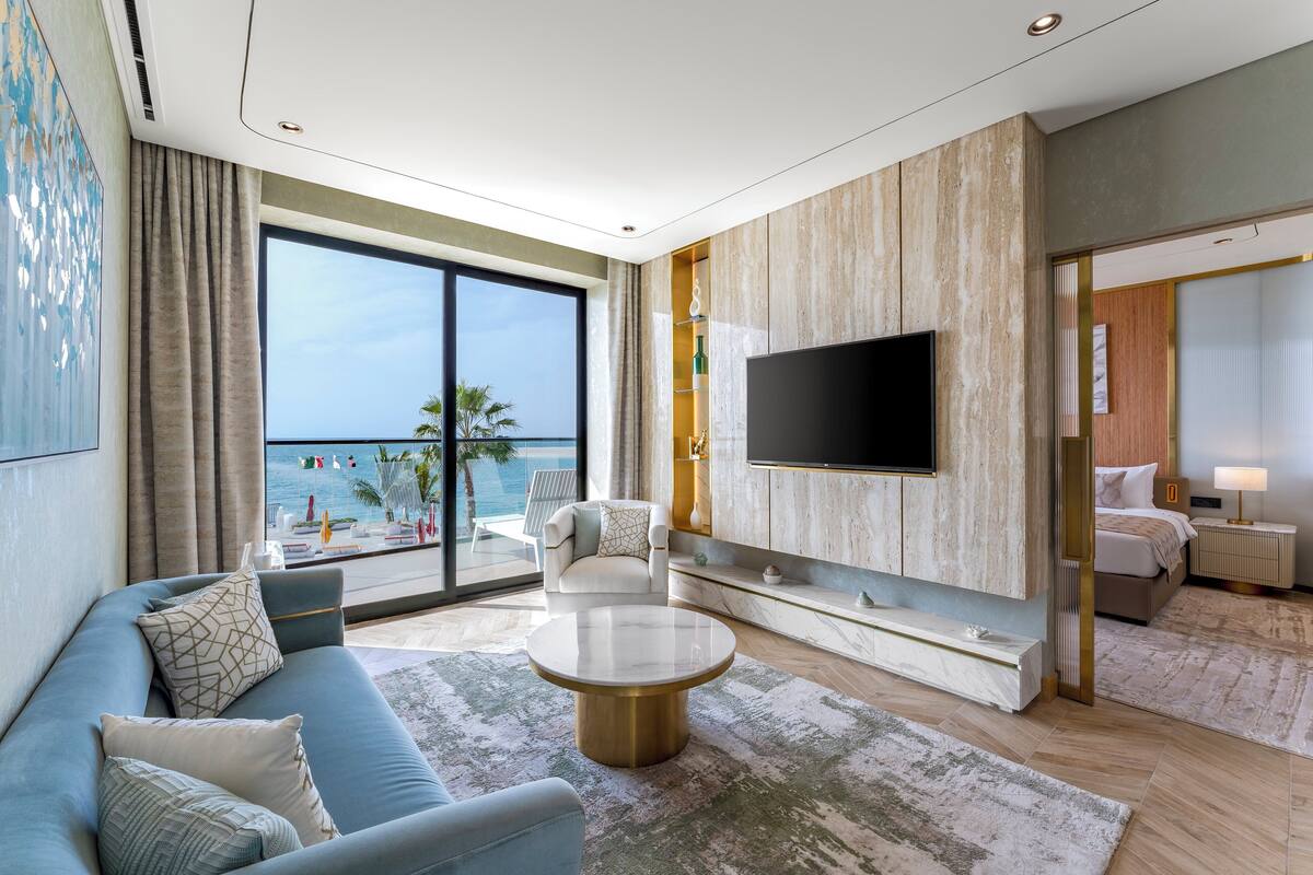 A modern living room with a large TV, comfortable seating, a view of the sea, and a balcony.