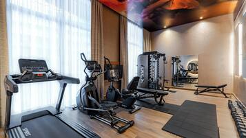 Een fitnessruimte met cardioapparatuur, krachttoestellen en een spiegel.