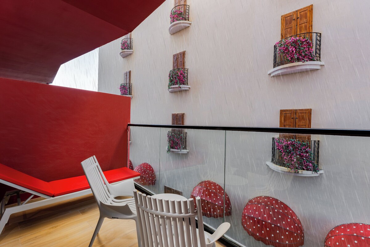 A modern interior with a red bench, white chairs, and a glass partition with red umbrellas.