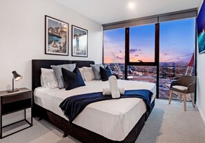 Une chambre moderne avec un grand lit, une table de chevet, une chaise et un téléviseur.