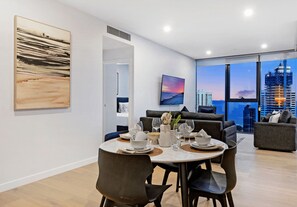 Un espace de repas moderne avec une table dressée pour quatre personnes, un canapé et une grande fenêtre donnant sur la ville.
