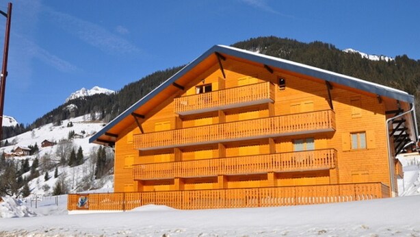A multi-story wooden building with balconies, set against a snowy mountain backdrop.