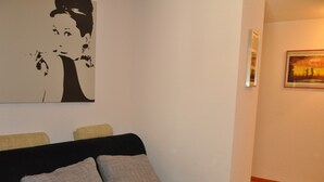 A living room with a black sofa, two grey cushions, a black and white artwork on the wall, and a framed picture on the adjacent wall.