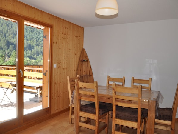 A wooden dining area with a table and chairs, a wooden ceiling, and a view of a forest through a glass door.