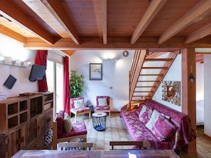 Une pièce chaleureuse avec des poutres apparentes, un ensemble de canapés, une table à manger et un escalier.