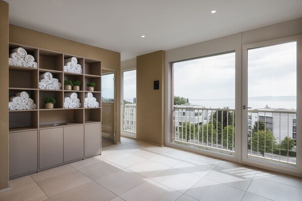Un balcón amplio con vistas a la ciudad y al mar, un estante empotrado con toallas y plantas, y una decoración interior moderna.