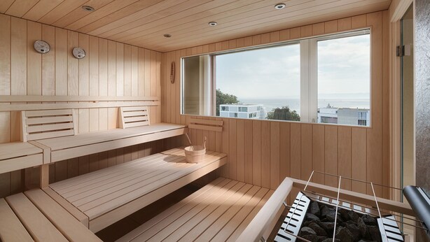 A sauna room with wooden benches, a large window, and a view of buildings and the sea. - bsmart hotel Arbon (Arbon)