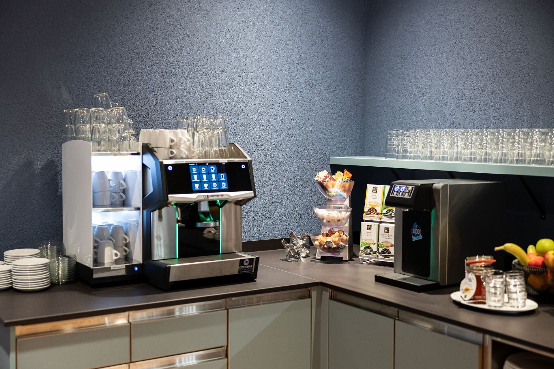 A coffee station with a coffee machine, a glass display, and a fruit bowl.