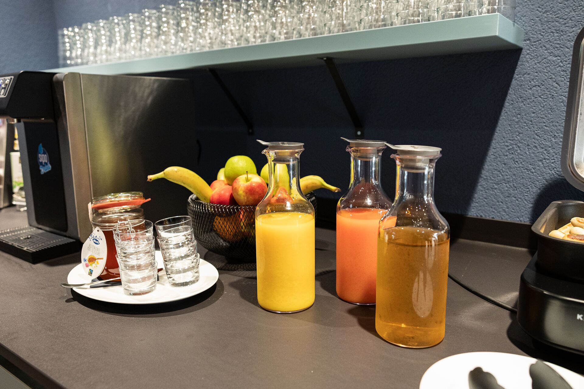 A breakfast setup with a fruit bowl, two glass bottles of juice, and a coffee machine.