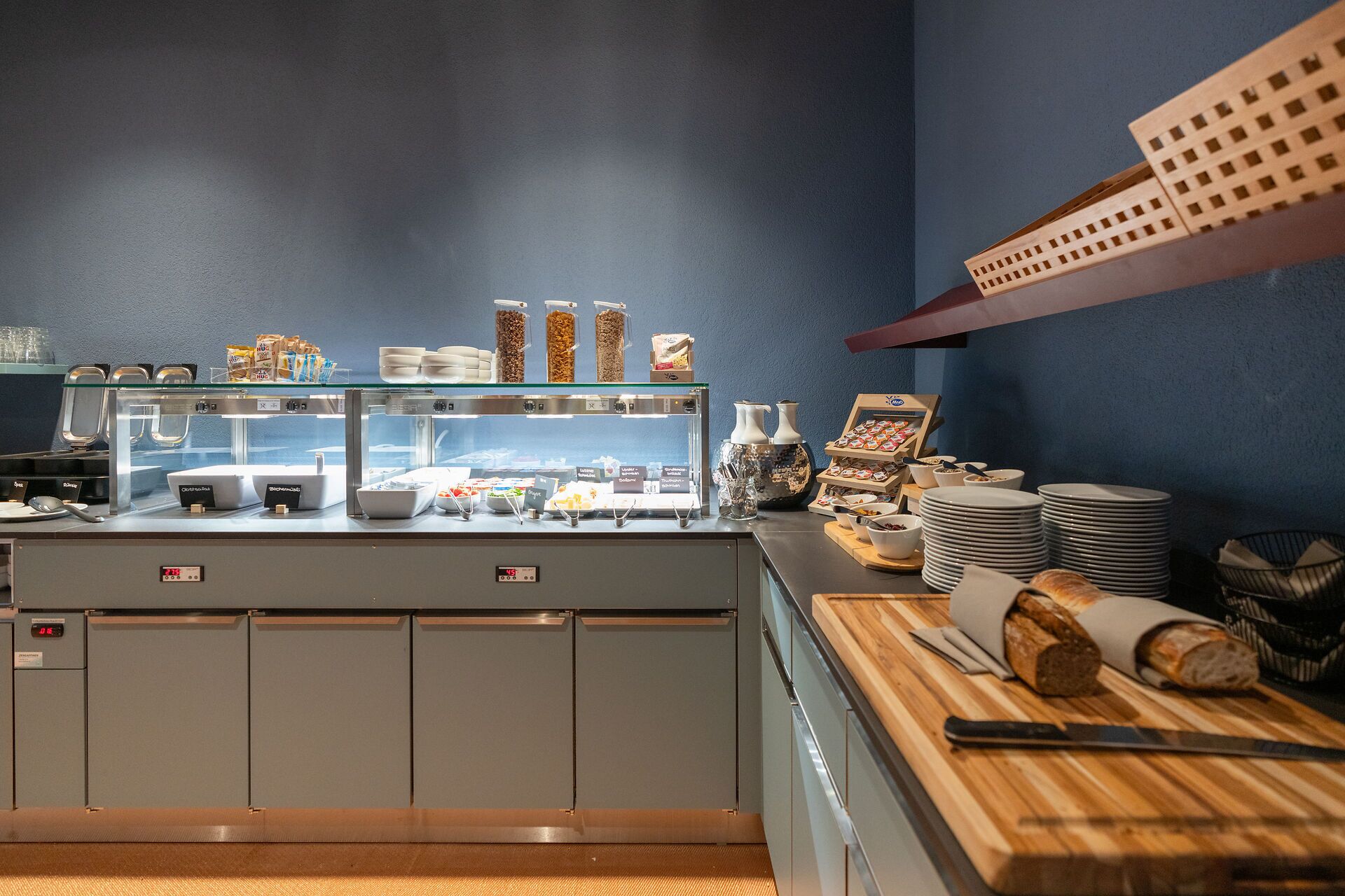 Uma área de buffet com diversos tipos de comida, um espaço para café e um balcão com pão e utensílios.