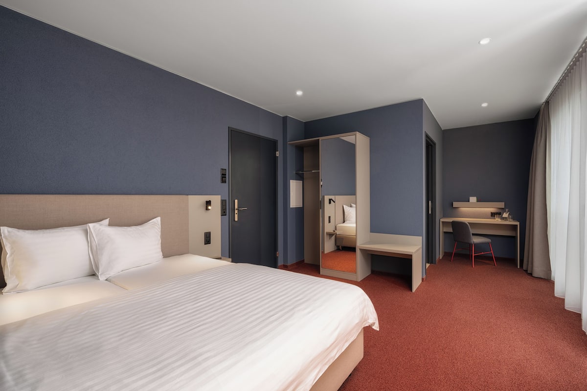 Una habitación de hotel con una cama grande, un escritorio y un espejo.