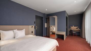 A hotel room with a large bed, a desk, and a mirror.