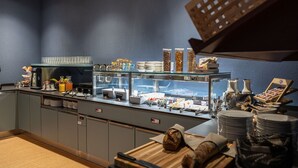 A buffet area with a variety of food items, a coffee machine, and a glass display case. - bsmart hotel Arbon (Arbon)
