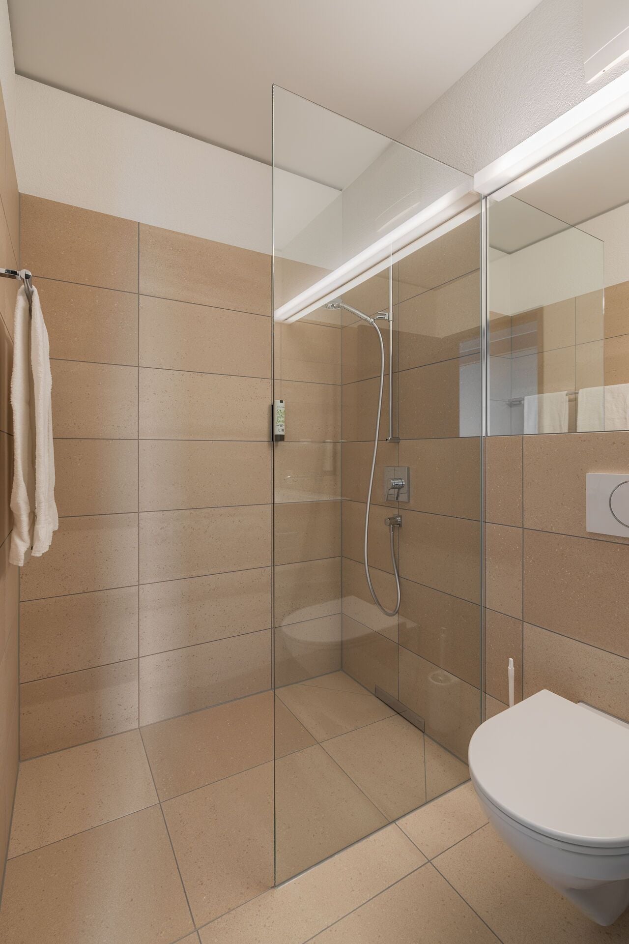 Un baño moderno con cabina de ducha de vidrio, inodoro y perchero.