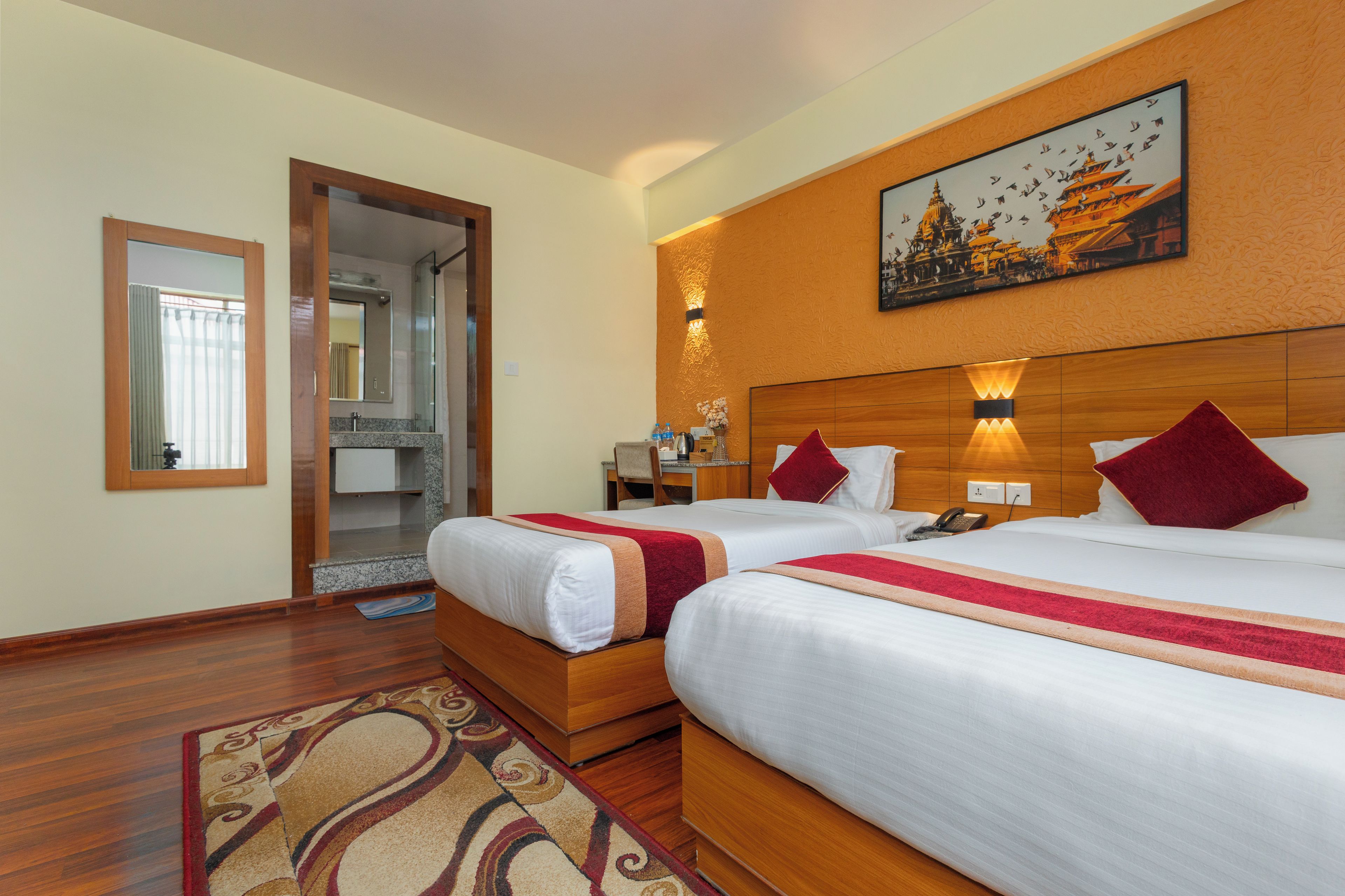 A hotel room with two beds, a bathroom, a painting of a temple, and a wooden floor.