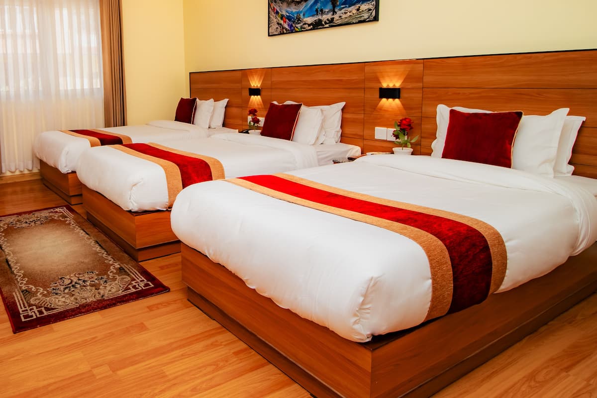 A hotel room with two beds, wooden headboards, a large painting, and a red and gold bed runner.