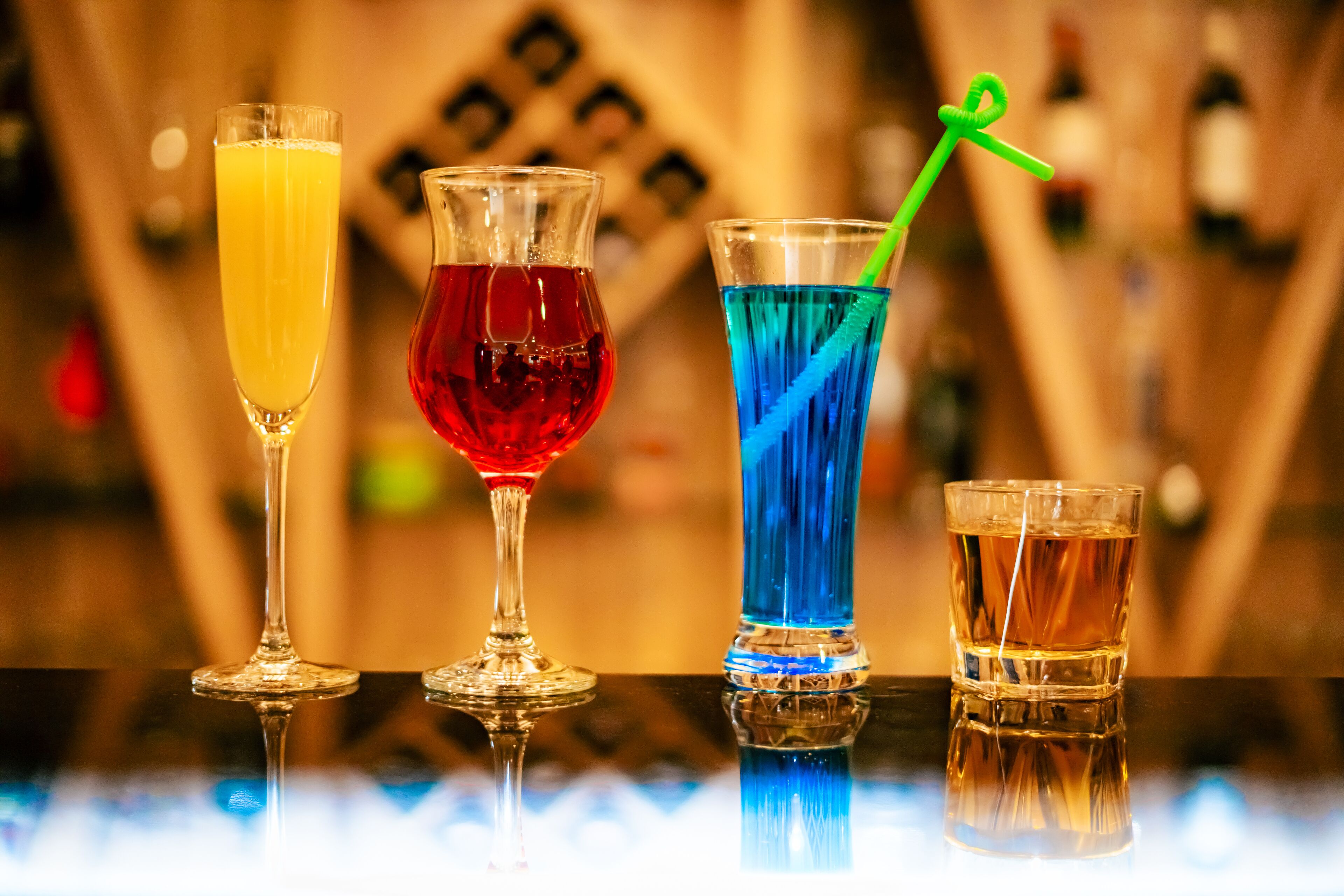 Quatre verres contenant différentes boissons, placés sur une surface réfléchissante.