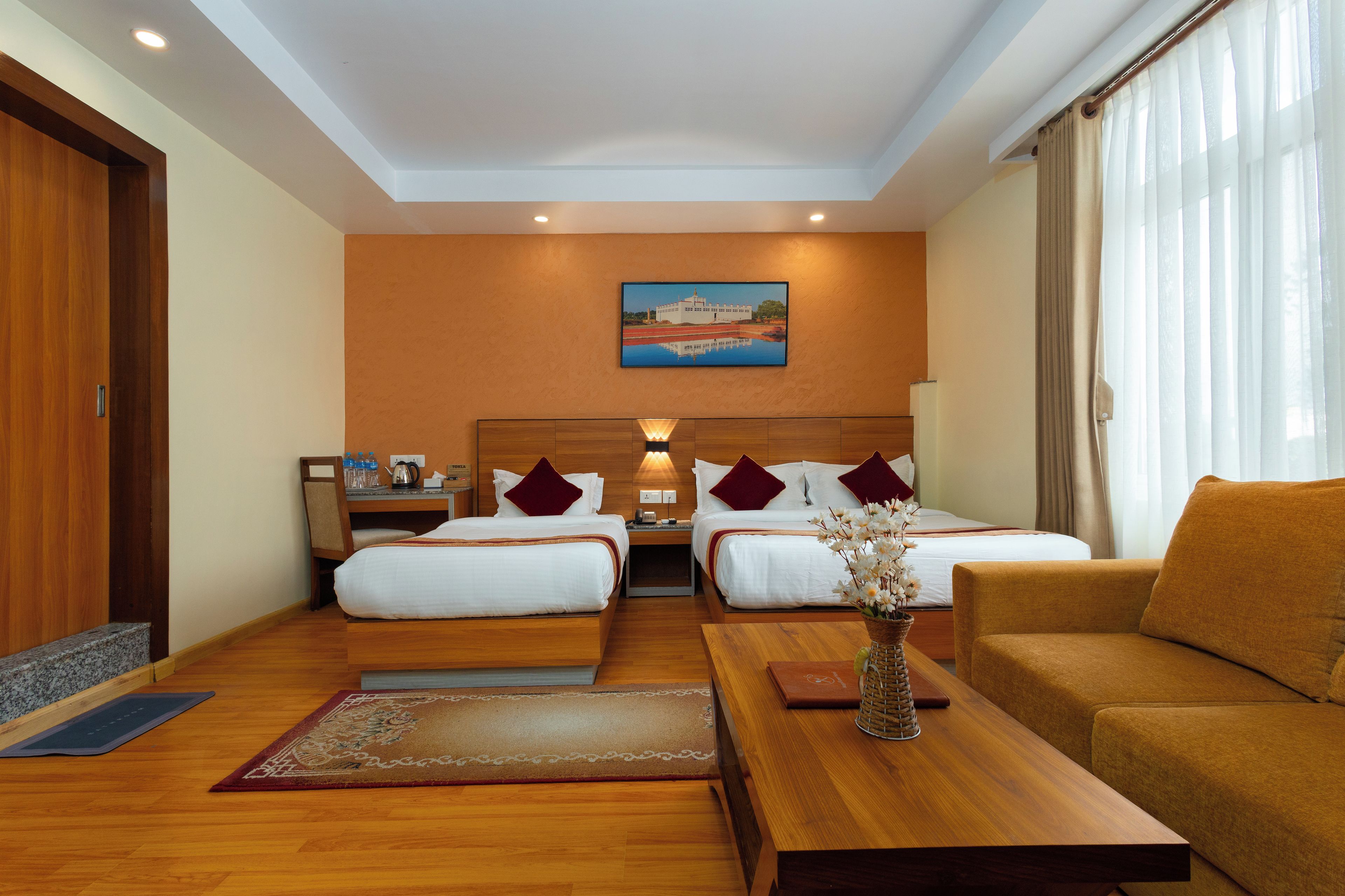 A hotel room with two beds, a sofa, a desk, and a painting on the wall.