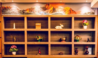 Una repisa de madera con varios objetos decorativos, como figuritas, flores y una pequeña casa en miniatura.