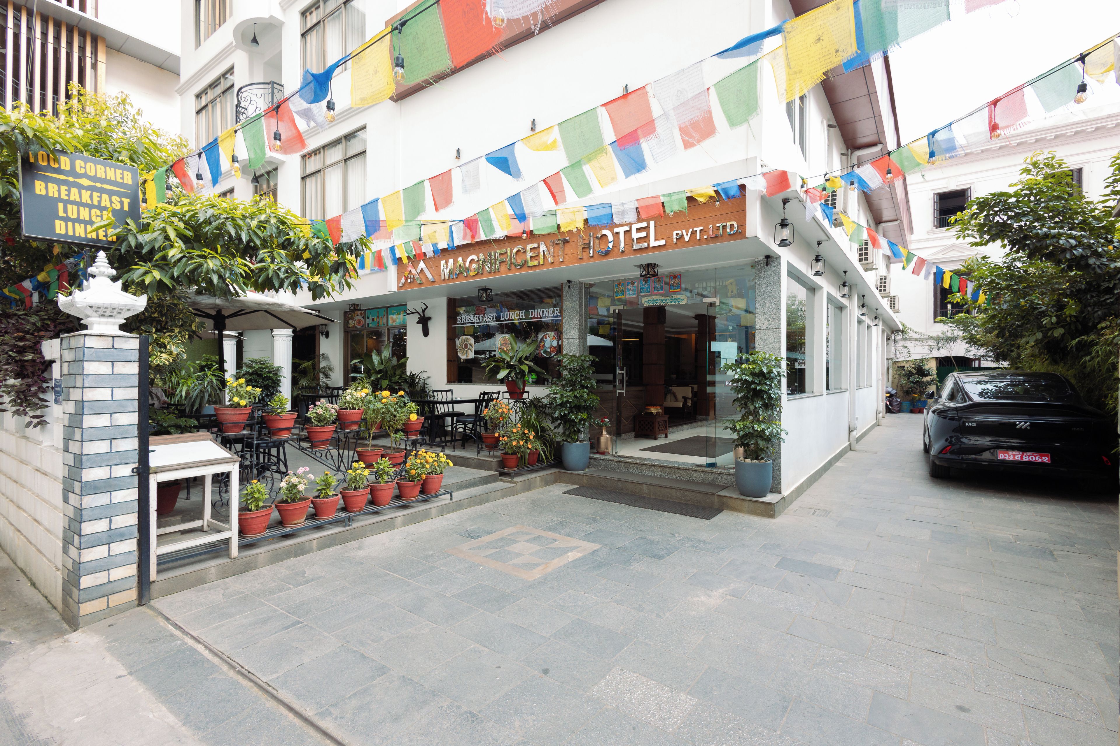 A hotel with a signboard, outdoor seating area with potted plants, and a staircase leading to the entrance.