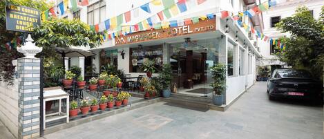 A hotel with a signboard, outdoor seating area with potted plants, and a staircase leading to the entrance.