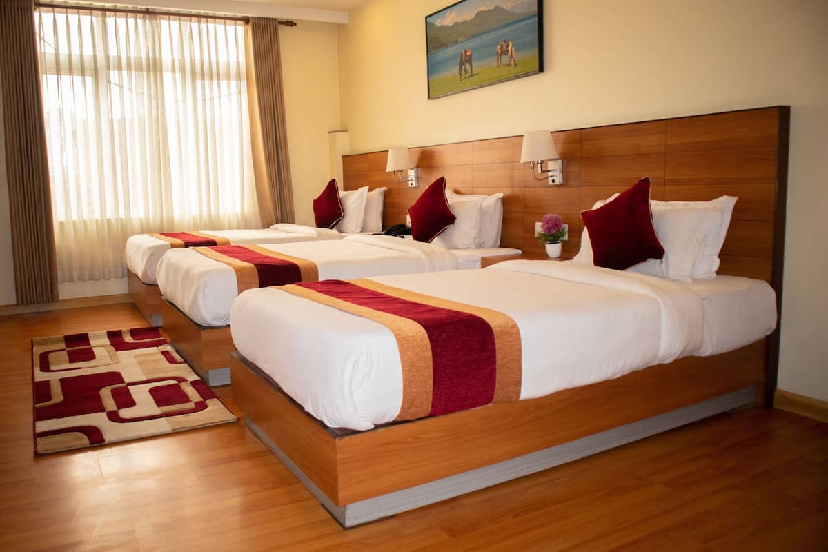 A hotel room with three beds, a wooden headboard, a painting on the wall, and a window with curtains.
