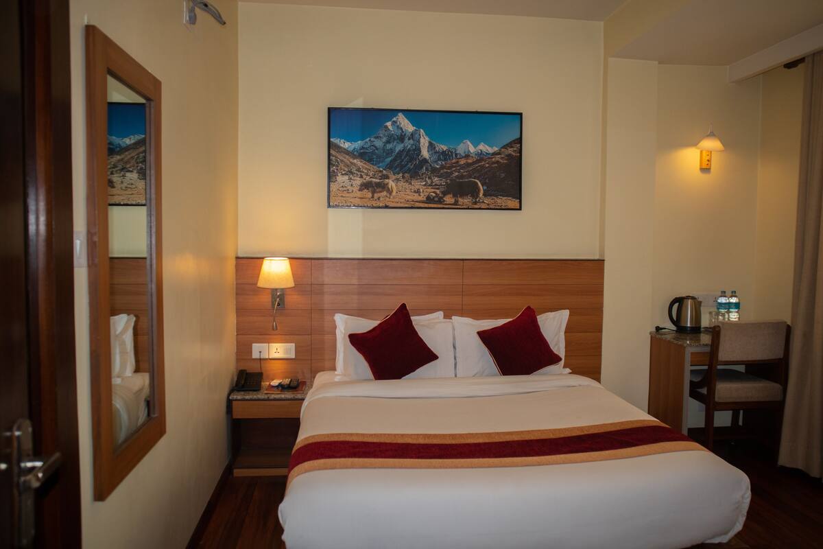 A hotel room with a bed, a nightstand, a lamp, a chair, and a painting on the wall.