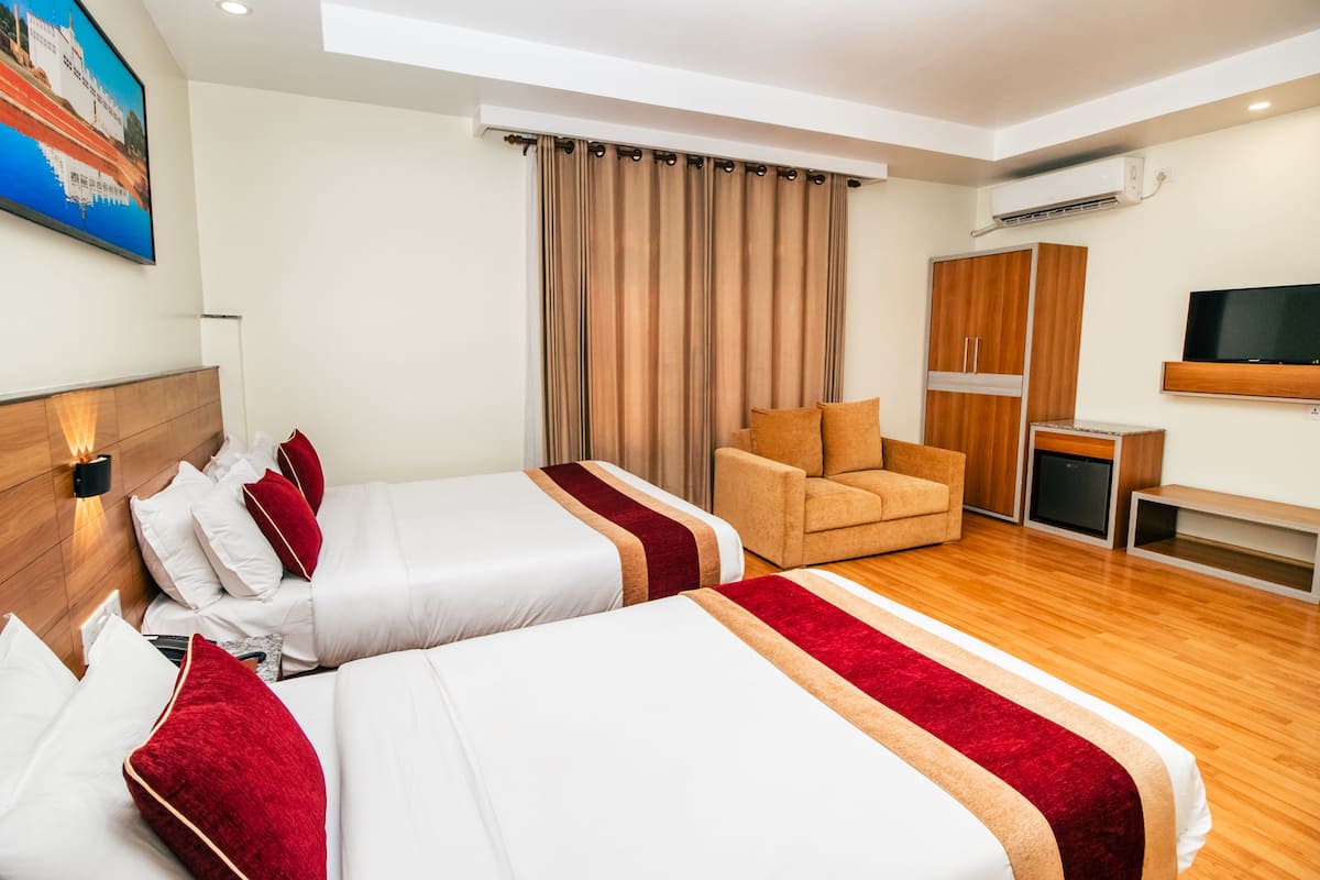 A hotel room with two beds, a sofa, a TV, and an air conditioning unit.