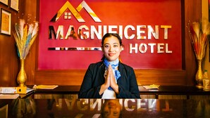 En receptionsdisk på Magnificent Hotel med en rød væg og et logo.