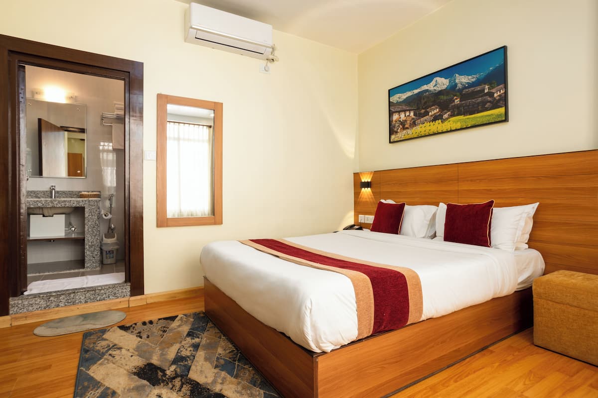 A hotel room with a wooden bed, a bathroom with a mirror, and a painting on the wall.