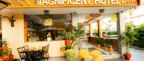 The exterior of the Magnificent Hotel with a clear view of the entrance, outdoor seating area, and potted plants.