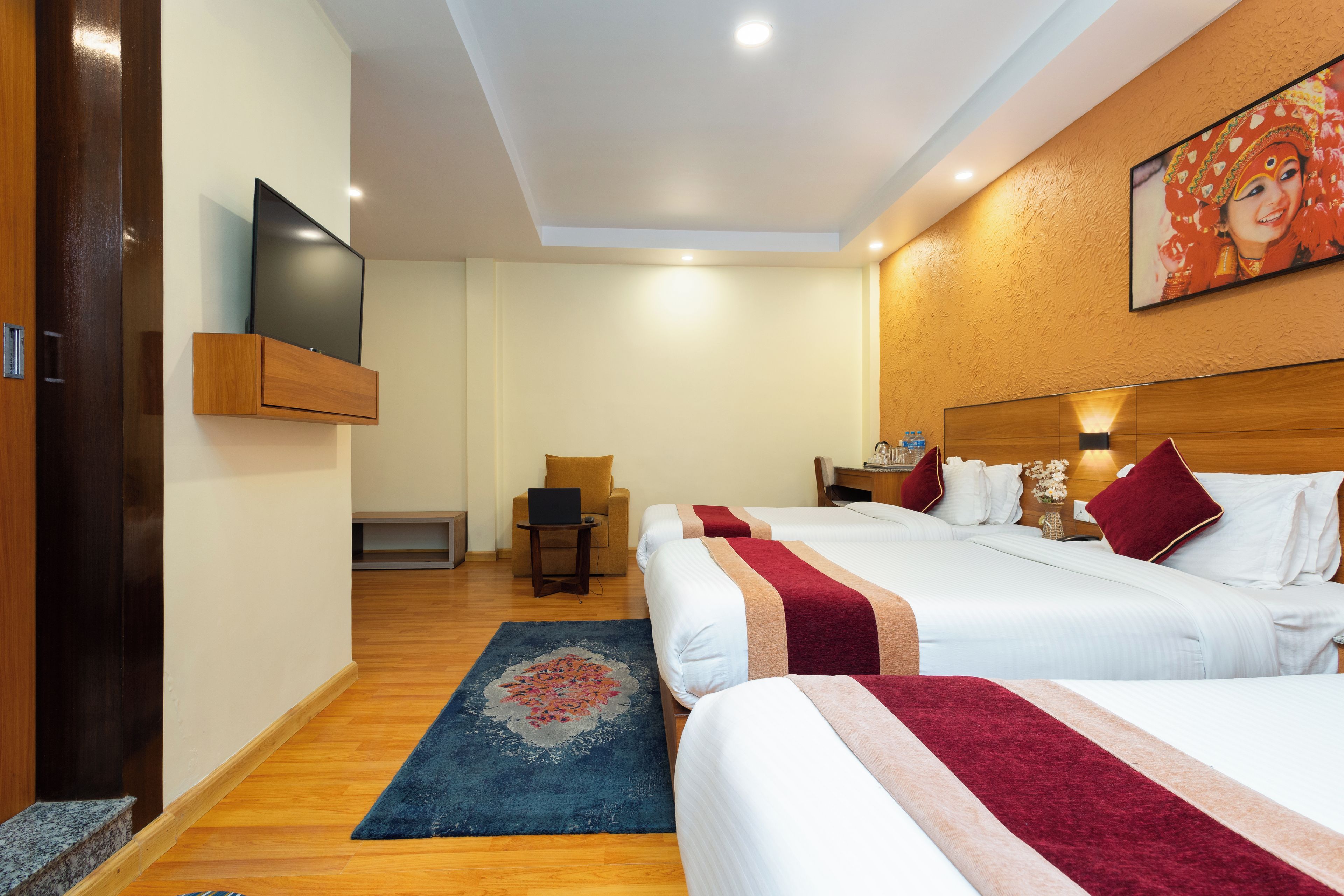 A hotel room with two beds, a television, a desk with a chair, and a small sitting area.