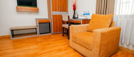 Un espacio habitable compacto con sofá, escritorio pequeño, televisor y kitchenette.