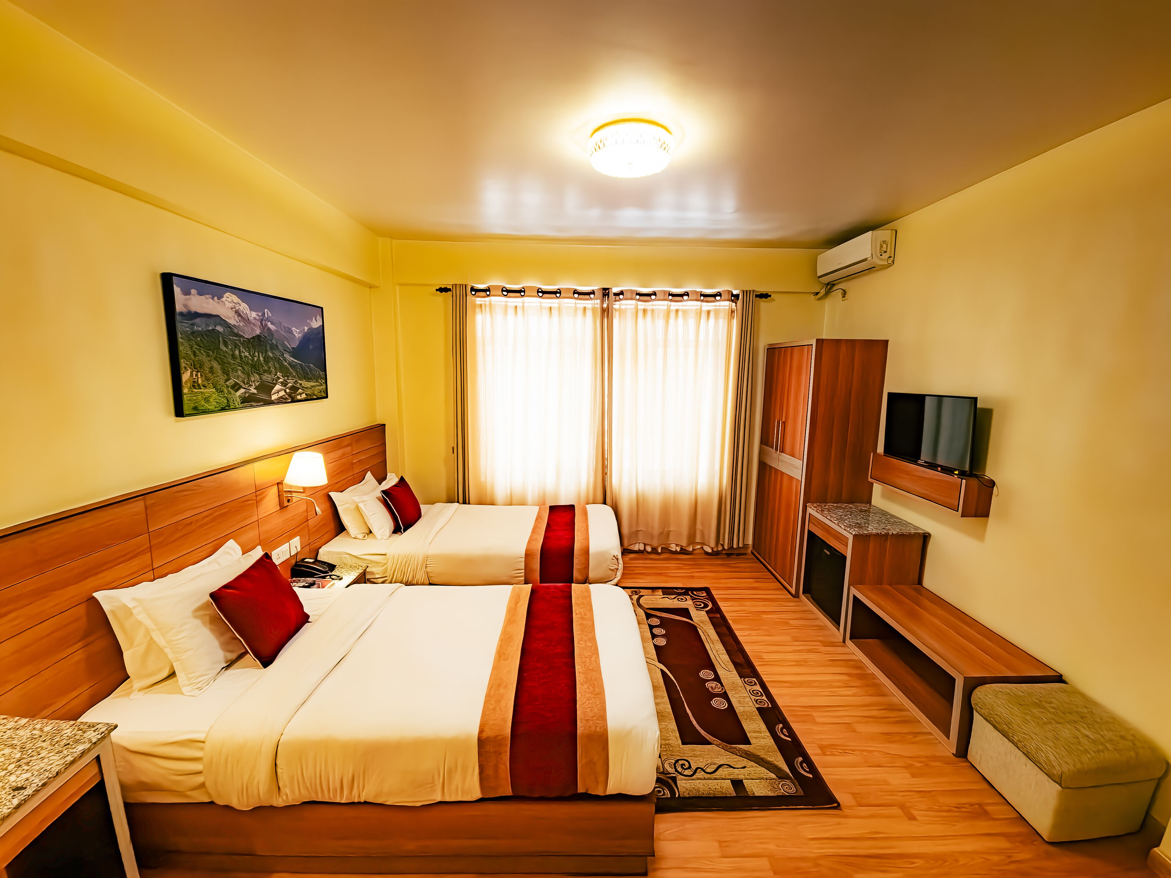 A hotel room with two beds, a TV, a desk, and a window with curtains.