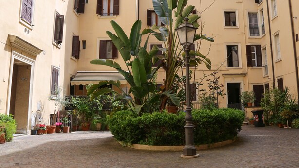 A courtyard with a central planter, potted plants, and a street lamp. - Mama House Roma (Rome)