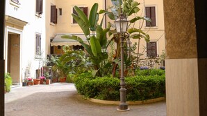 A cobblestone courtyard with a large plant in the center, surrounded by buildings with multiple windows and shutters. - Mama House Roma (Rome)