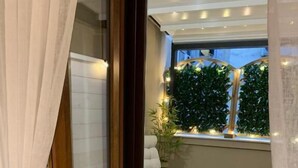 A room with a sliding glass door leading to an outdoor area with a white chair, a patterned rug, and a green plant. - Mama House Roma (Rome)