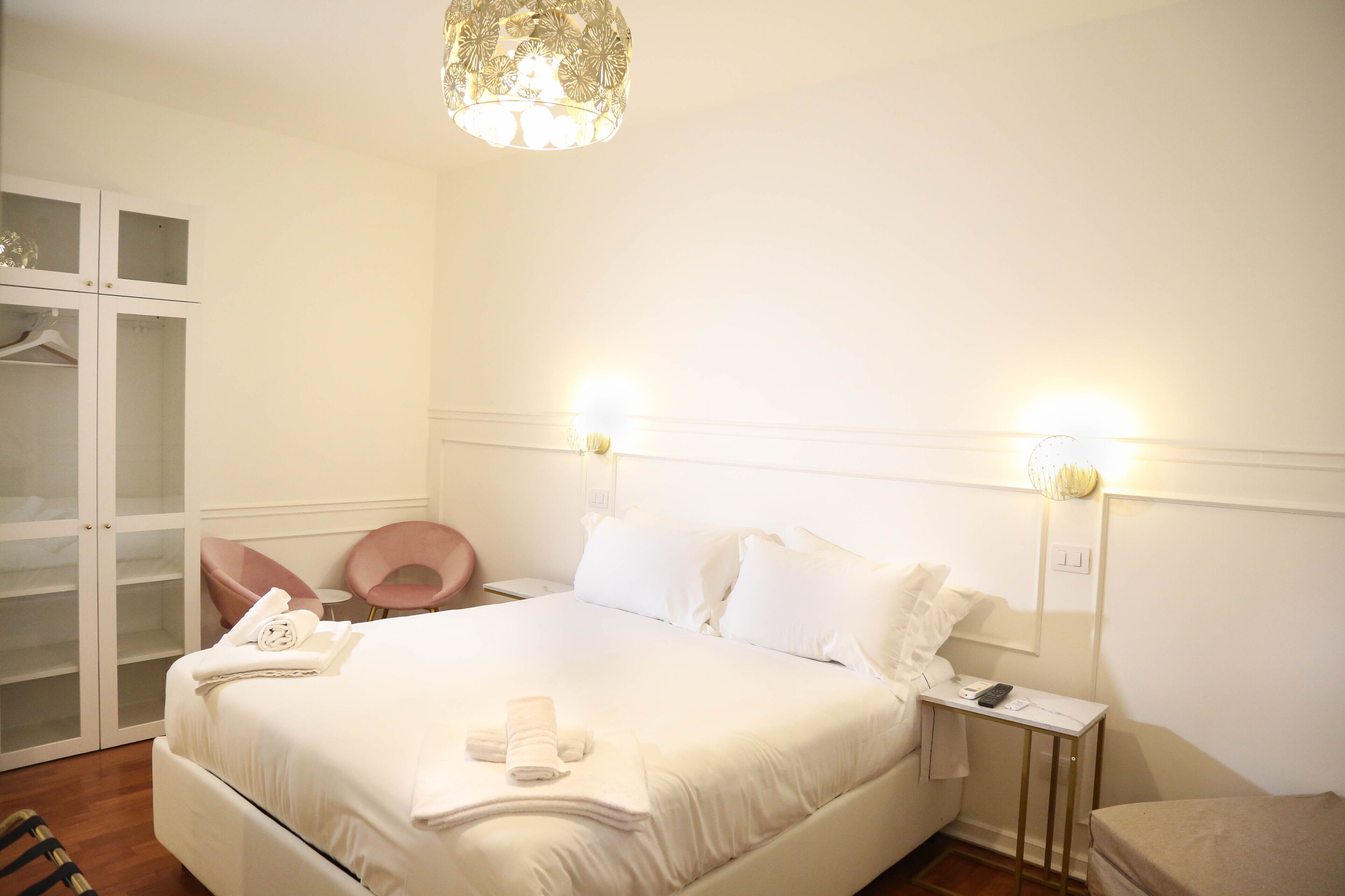A neatly arranged hotel room with a large bed, bedside tables, a wardrobe, and a hanging chair.