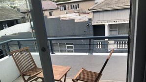 A balcony with two wooden chairs and a small table, overlooking a residential area with houses and a building with a sign. - Beautiful Newly Renovated Penthouse in the Trendy Gardens Surbub (Cape Town)