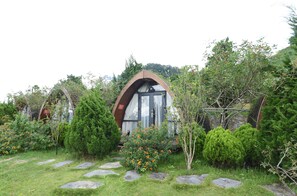 Un chalet accueillant, doté d’une entrée arquée originale, entouré d’une végétation luxuriante et accessible par un sentier en pierre.